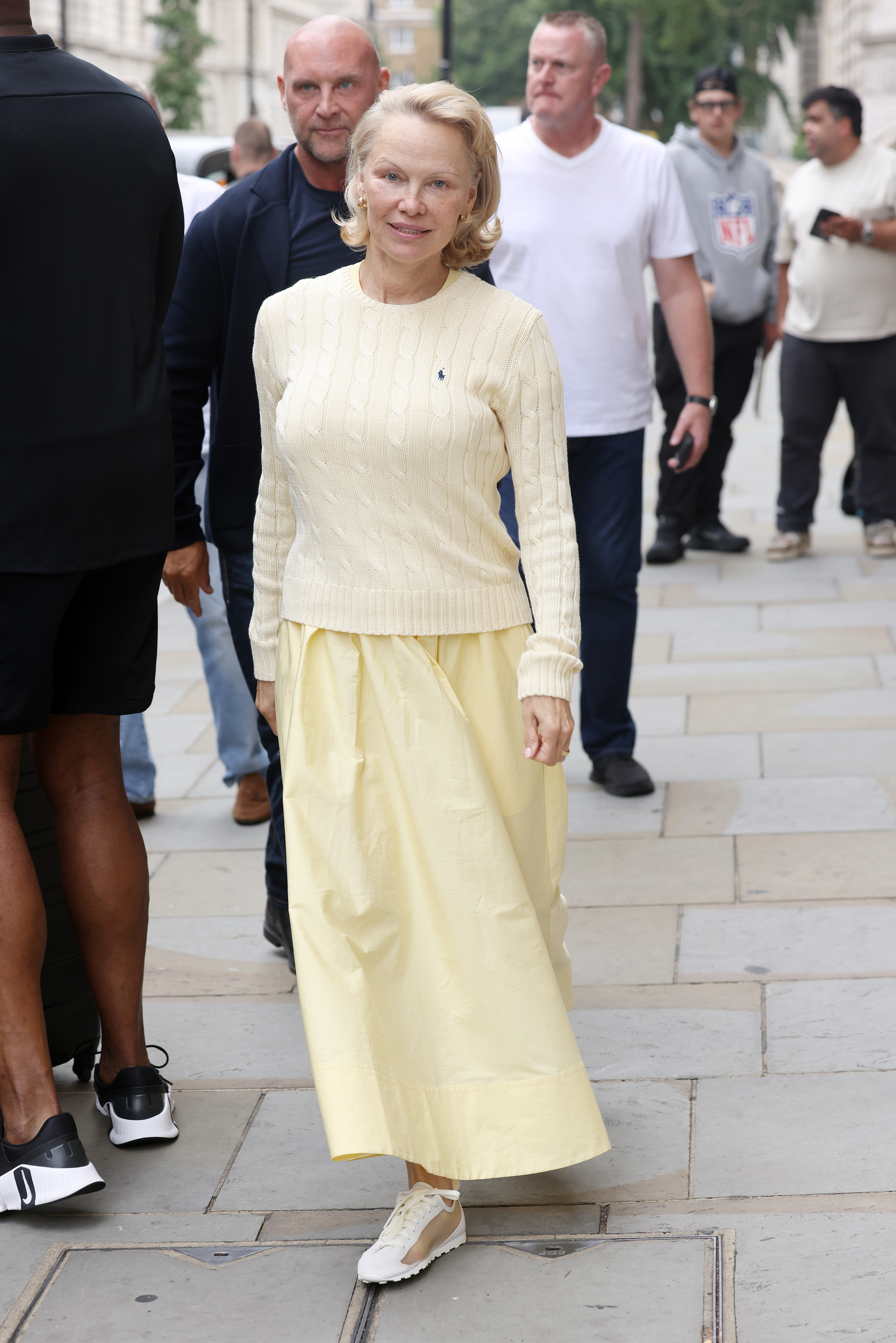 Pamela Anderson wears a yellow knit and yellow maxi skirt with white and gold trainers.