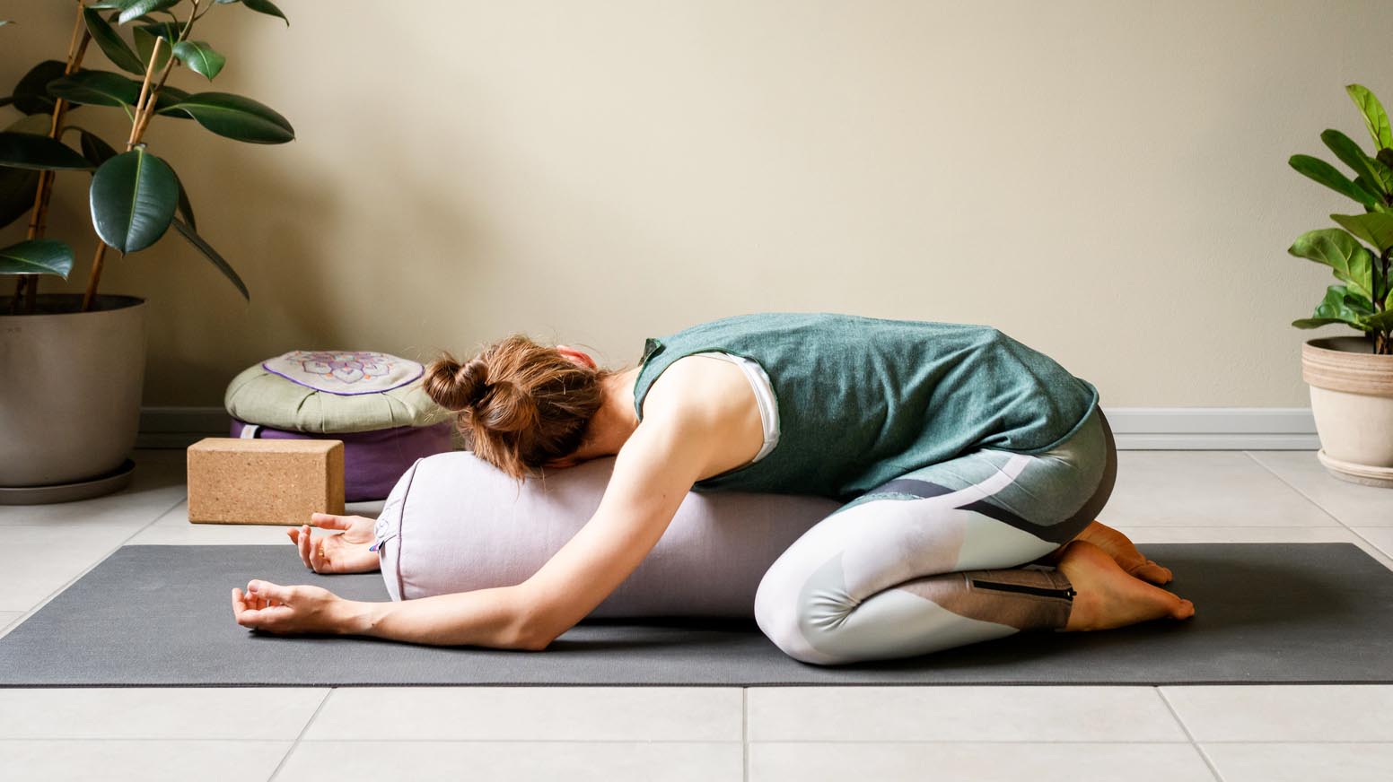 a woman doing child&#039;s pose on a bolster