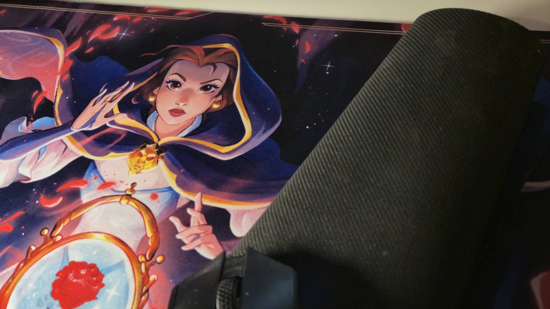 Photo of a Lorcana playmat featuring Belle from Beauty and the Beats, with another playmat rolled up and sitting on top.
