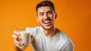 A man holds out a glass of a white substance that may well be mayonnaise.