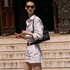 Fashion week attendee wearing sunglasses, white button down shirt, shoulder bag, and white shorts
