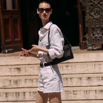 Fashion week attendee wearing sunglasses, white button down shirt, shoulder bag, and white shorts