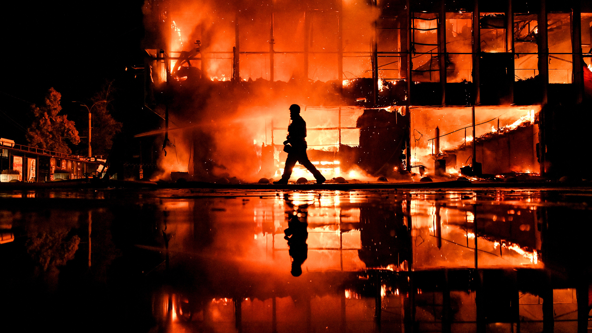 A firefighter is silhouetted against a blaze at the Intrade shopping centre following a Russian drone attack in Zaporizhzhia, Ukraine