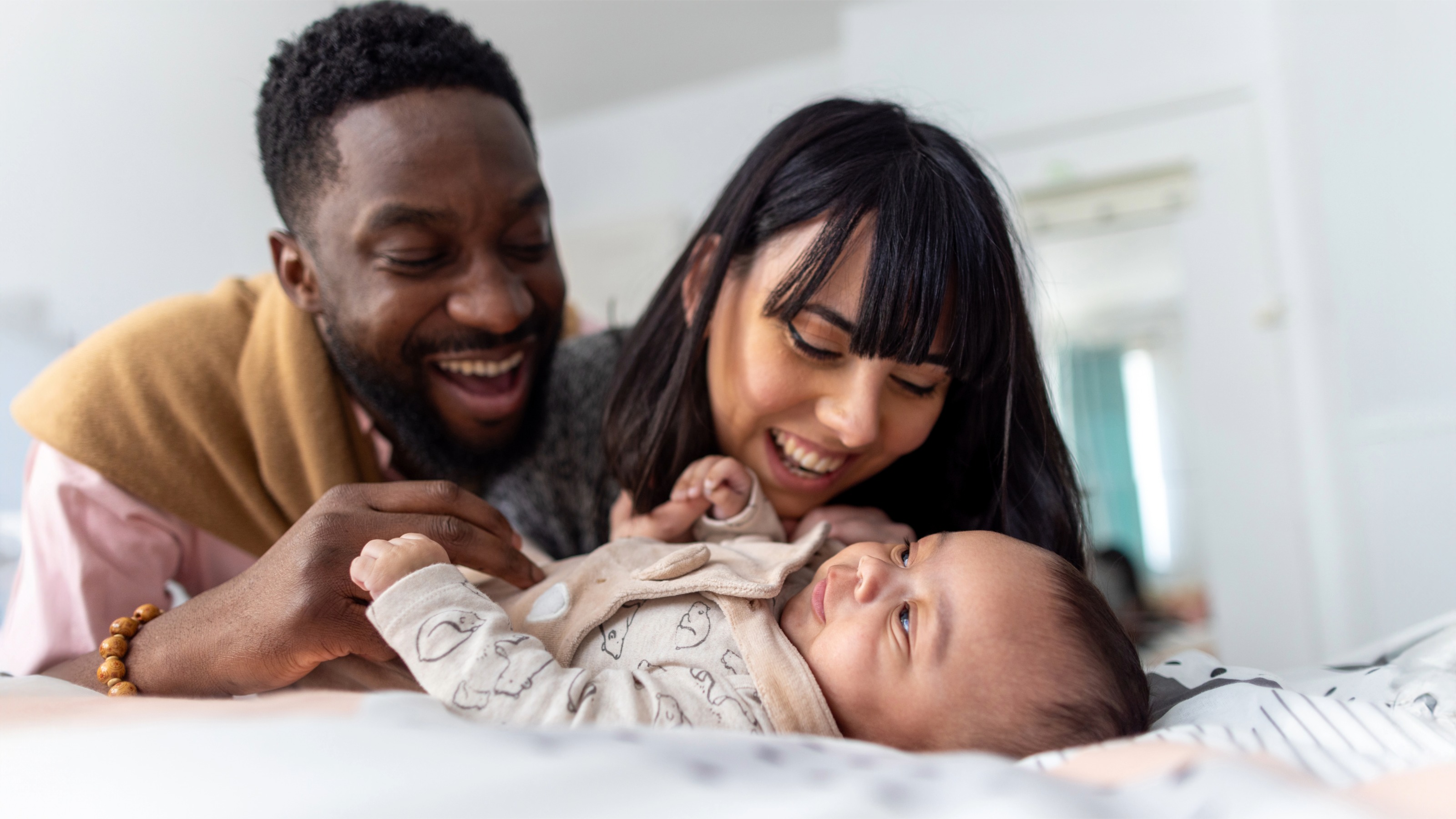 New parents smiling and looking over their baby lying on a bed