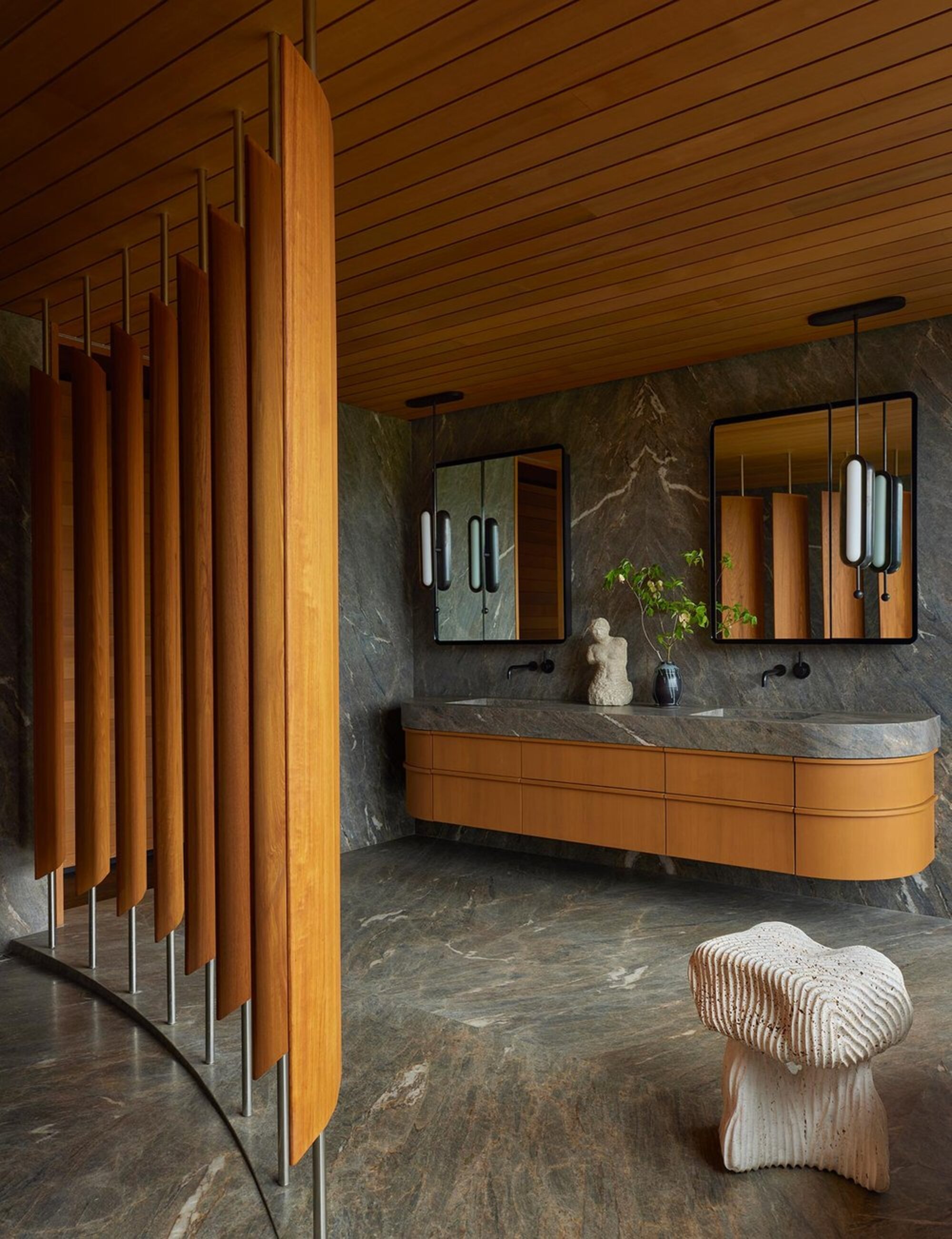 mid-century modern bathroom with gray marble floors, walls, and countertop, curved timber vanity, timber panelled ceiling, and timber screen, two mirrored cabinets, and a sculptural stool