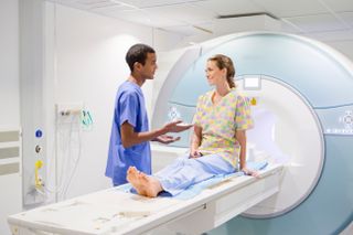 Woman talking with a nurse while sitting on a table for an MRI machine