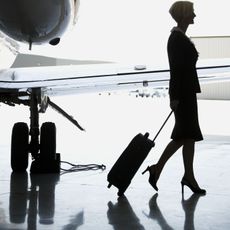 Flight attendant in high heels with wheelie bag next to plane