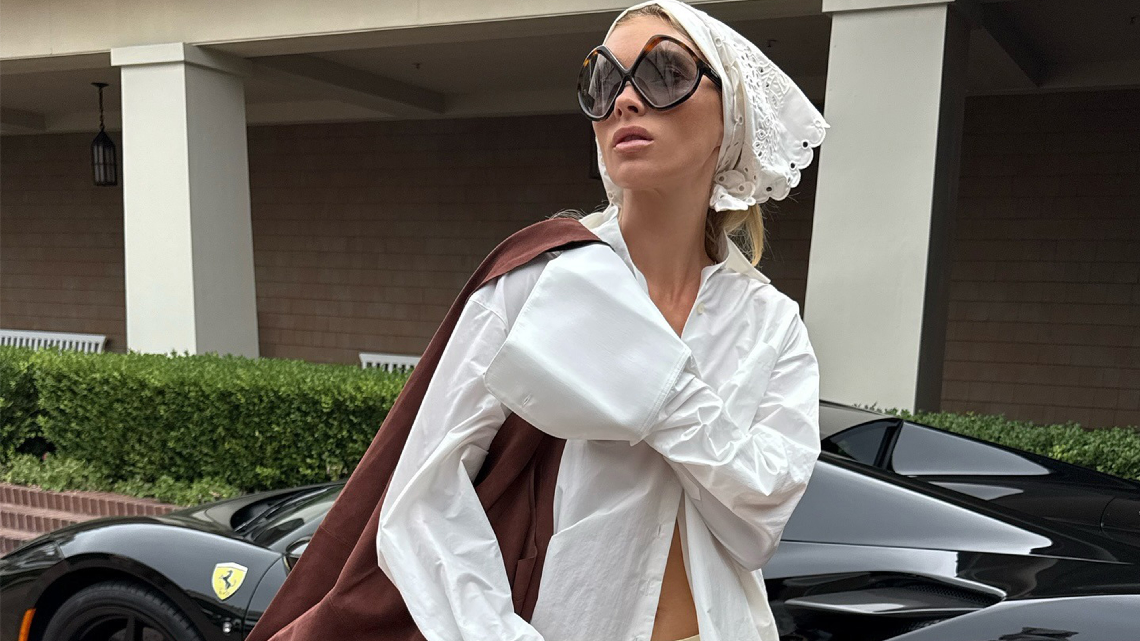 Elsa wears a white head bandana, brown suede bag, white button-down, ivory silk pants, and tan sandals.