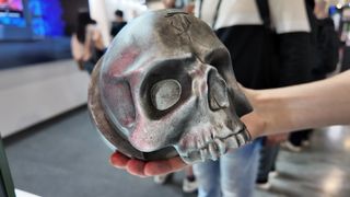 A hand holds a fake, metallic skull marked with a rune found throughout Doom: The Dark Ages.