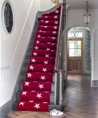 Red stair runner with star motif on black stairs in hallway with Herringbone effect wooden flooring