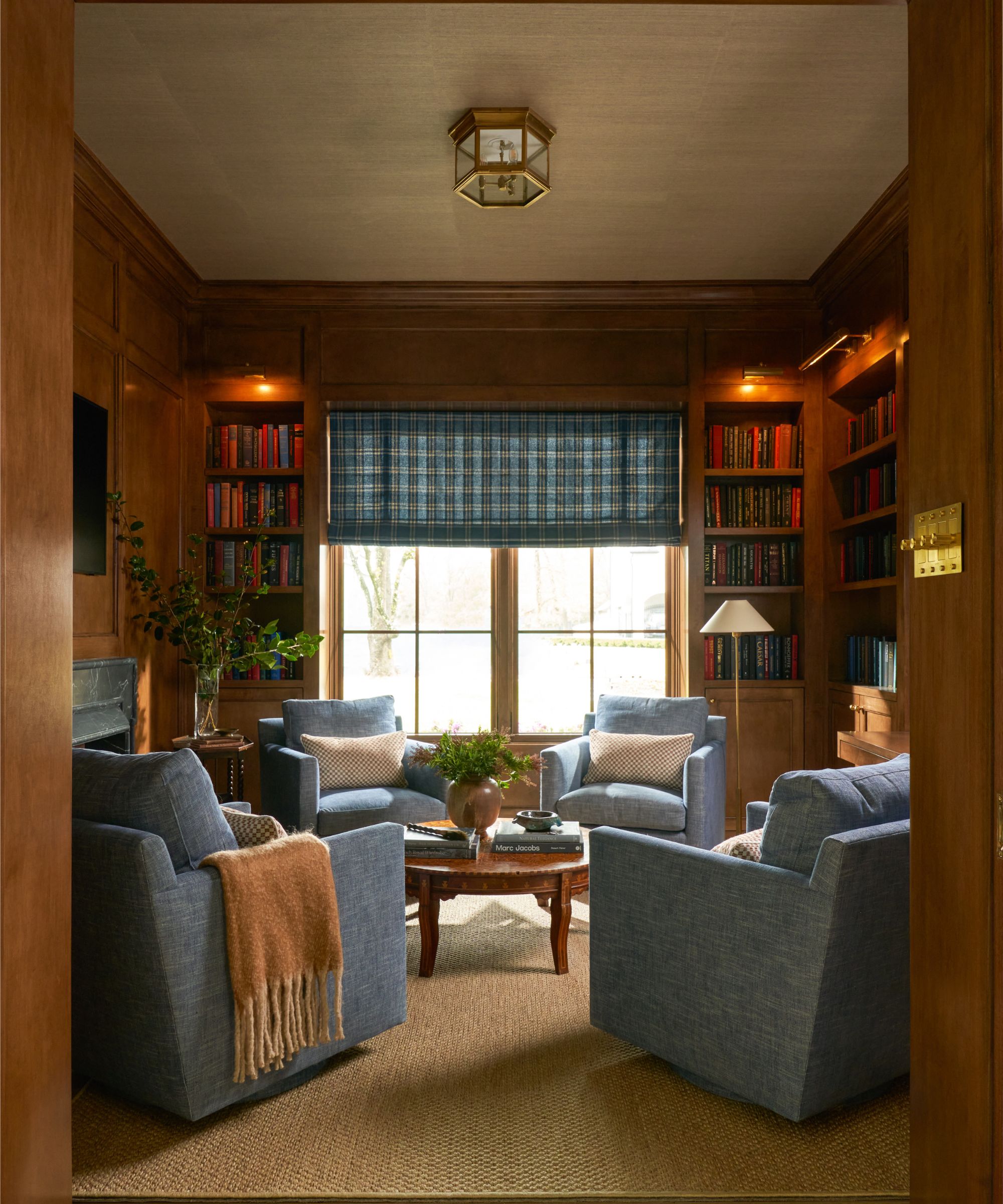 Cozy living room with wood willwork, ambient wall lighting, blue armchairs and blue check roman blind
