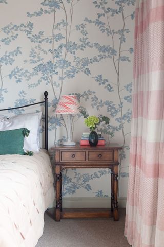 cast iron bedhead with blue leaf print wallpaper and pink checked curtains