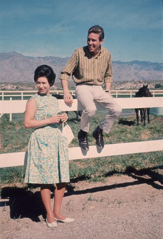 A 1965 photo of Princess Margaret leaning against a white fence in the mountains while her husband sits on a railing