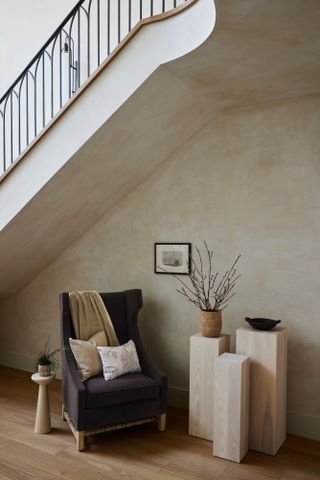 A travertine side table and an upholstered armchair are located at the bottom of the stairs