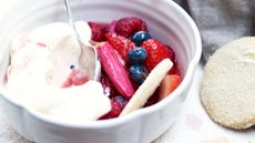 red berry and rhubarb compote with orange blossom syllabub in a bowl with a biscuit in the bowl and another biscuit to the side of it