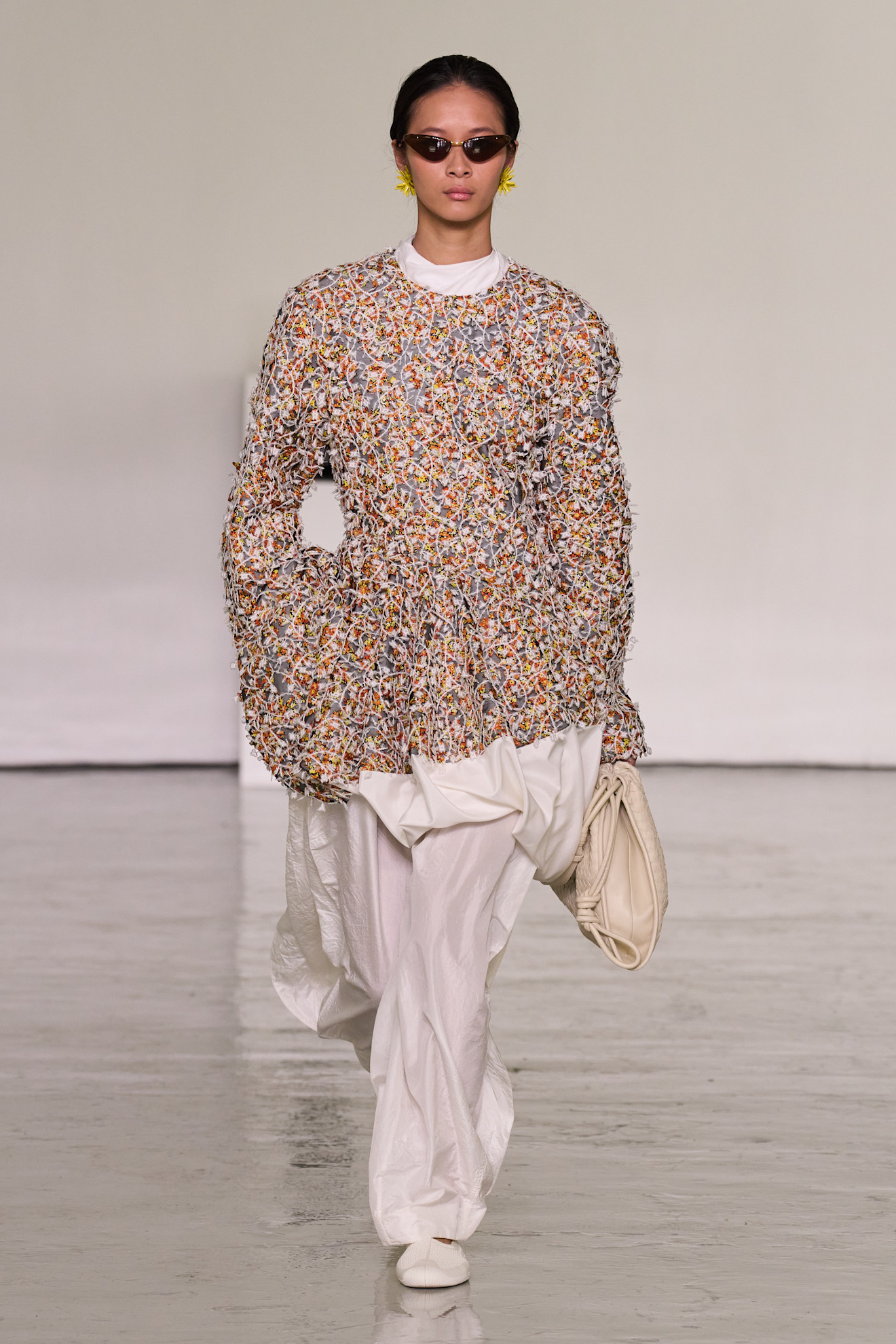 A model walking in the spring/summer 2027 Bottega Veneta show during Milan Fashion Week wearing an embroidered top with white poplin pants.