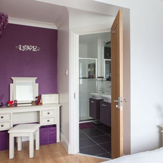 dressing room with purple wall and white table with stool and wooden door