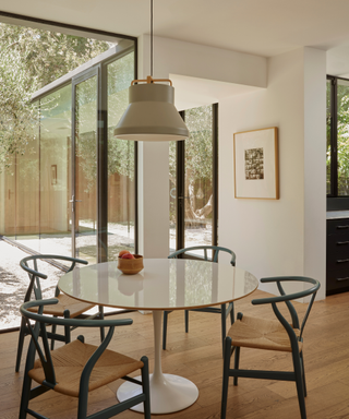 Dining table table and four chairs in mixed materials in contemporary home with glazed windows letting natural light pour in