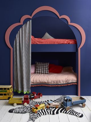boy's bedroom with beds in an alcove, stripe drape, coral bedding, white painted floorboards, wooden toys