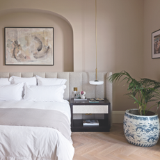 Warm, pale pink bedroom with large houseplant, white bedding and alcove.