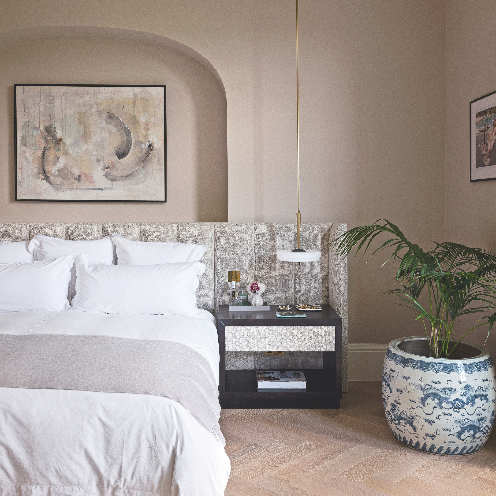 Warm, pale pink bedroom with large houseplant, white bedding and alcove.
