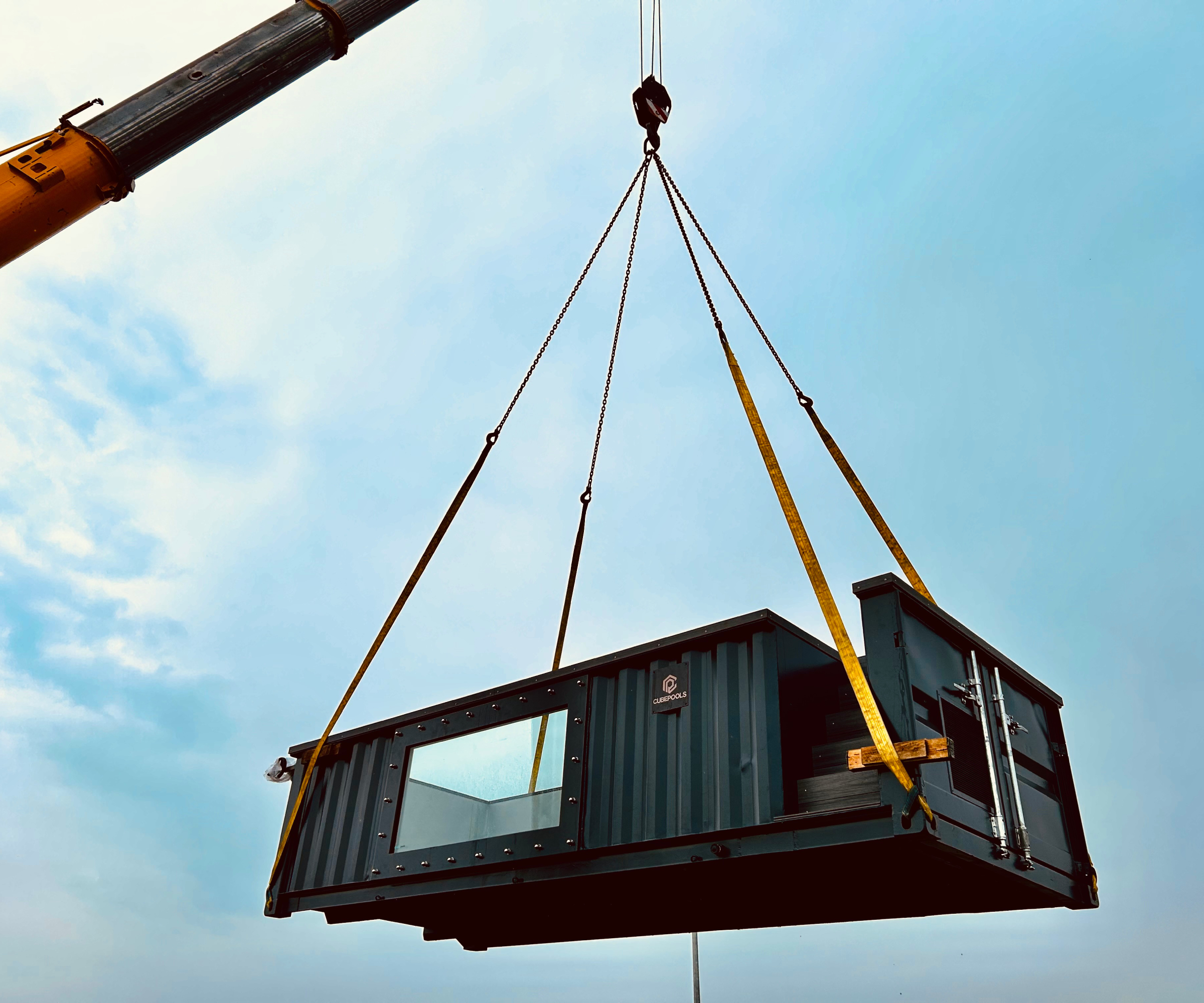 shipping container pool hanging at height from crane