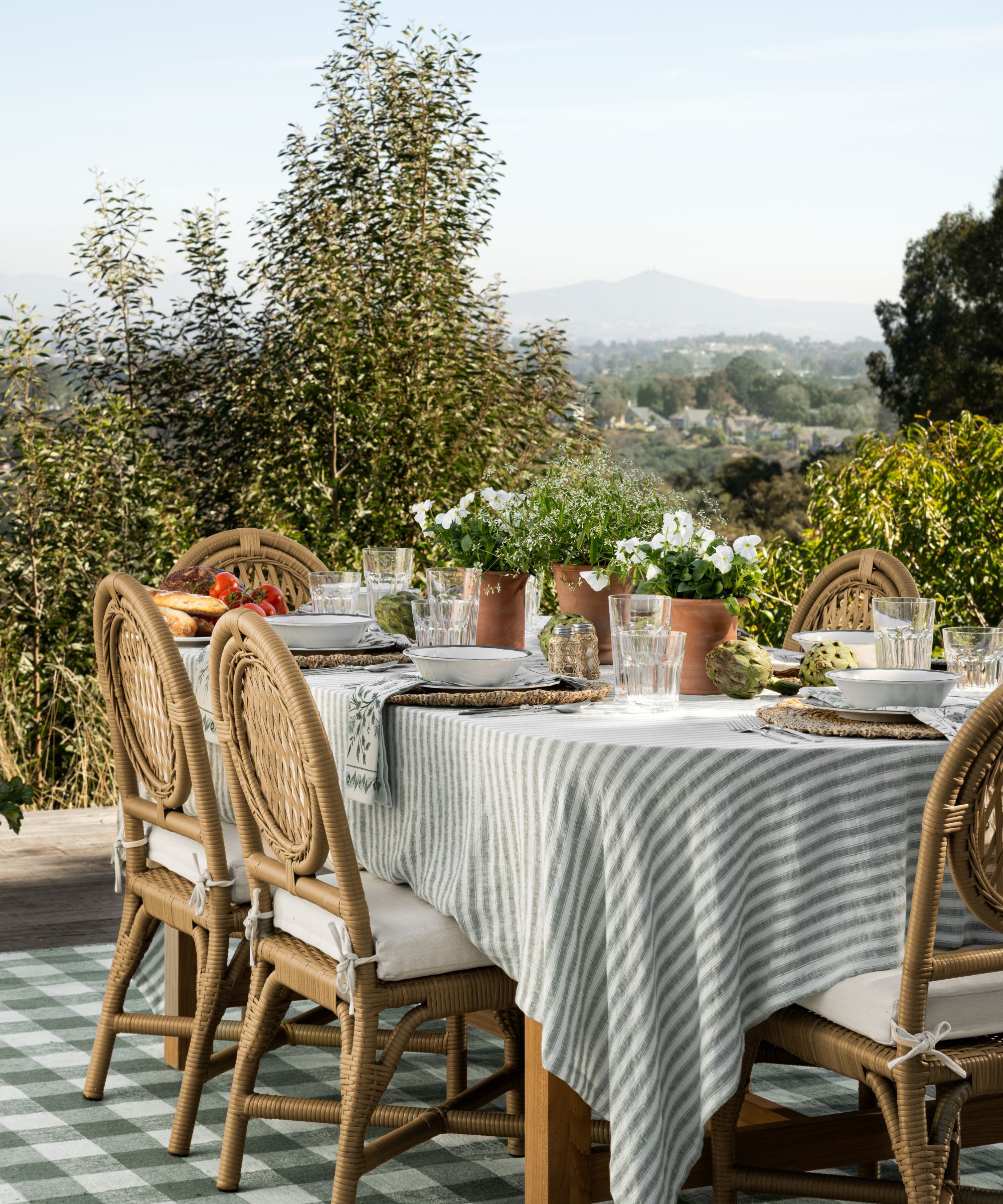 Summer garden table by Studio McGee featuring a striped linen table cloth, rattan place mats and terracotta pots filled with white flowering plants
