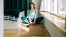 Woman sitting on cork yoga mat in living room in front of window in sunshine