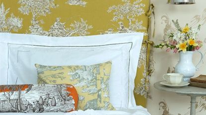 yellow bed with design cushions and flower pot on bedside table