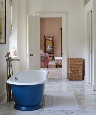 An example of how to design a bathroom showing a blue freestanding bath on a marble floor