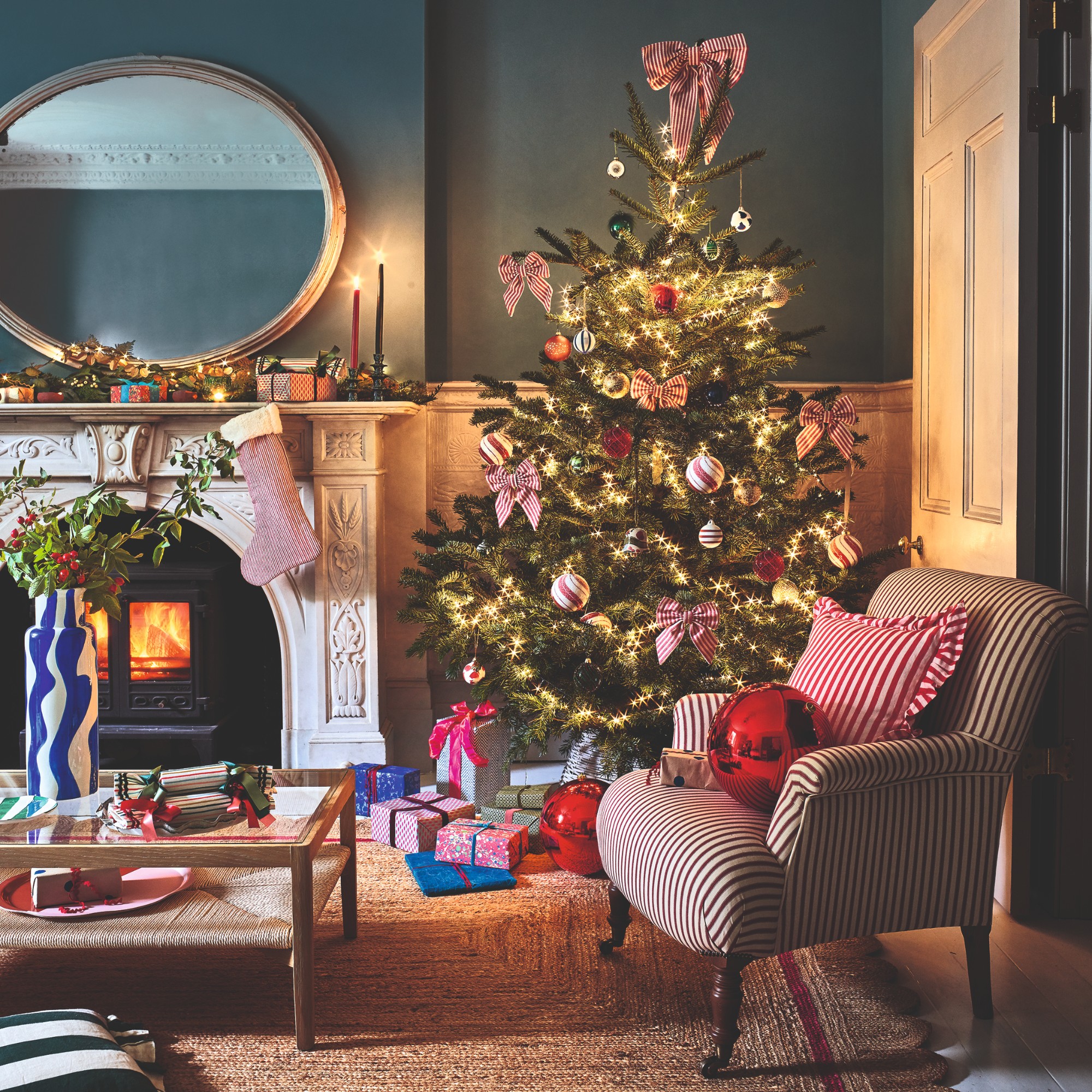 A living room decorated for Christmas with a lit-up tree and a garland with Christmas lights on the mantelpiece