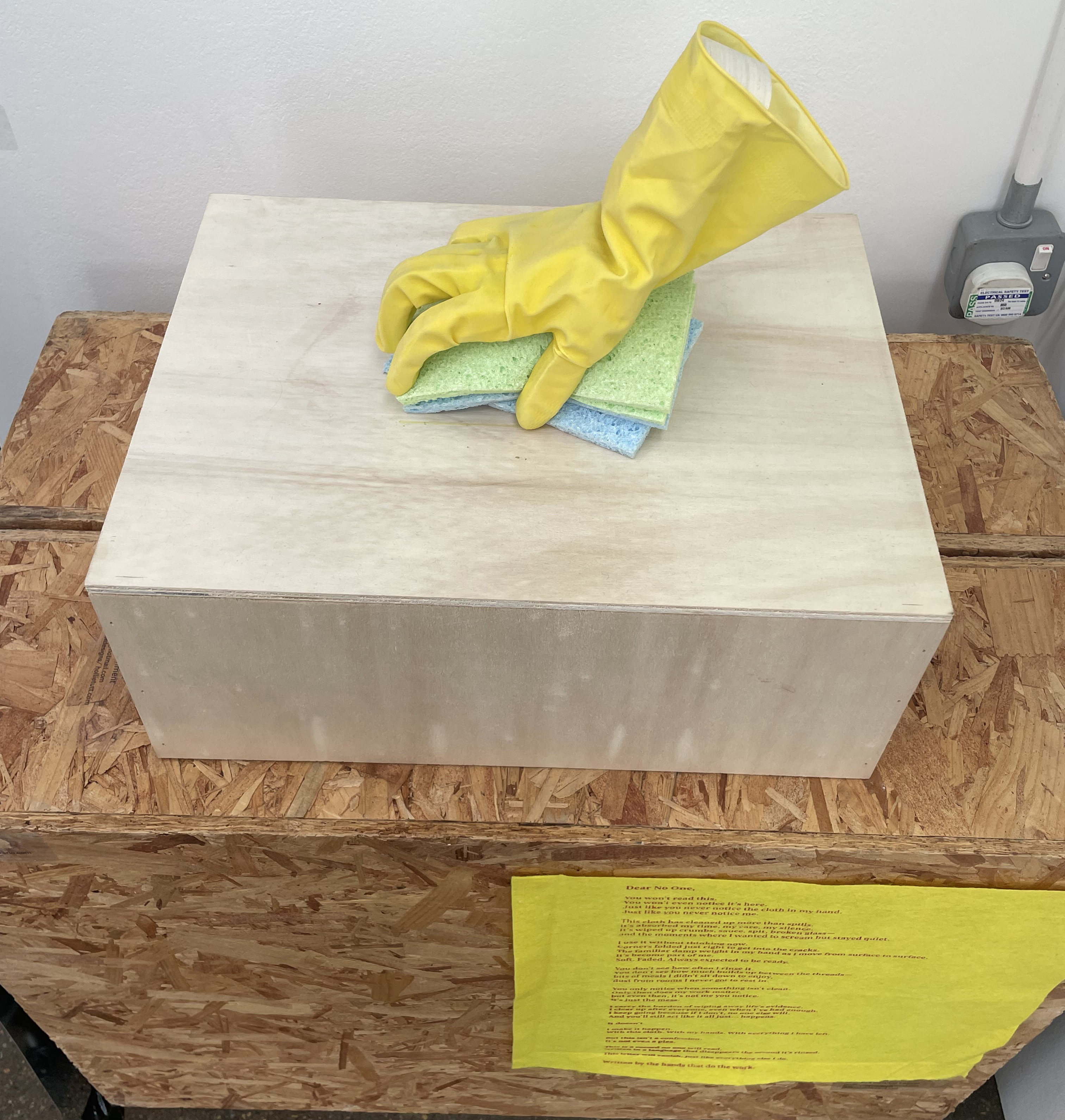 gloved hand cleaning on a plinth and a poem on a washcloth below