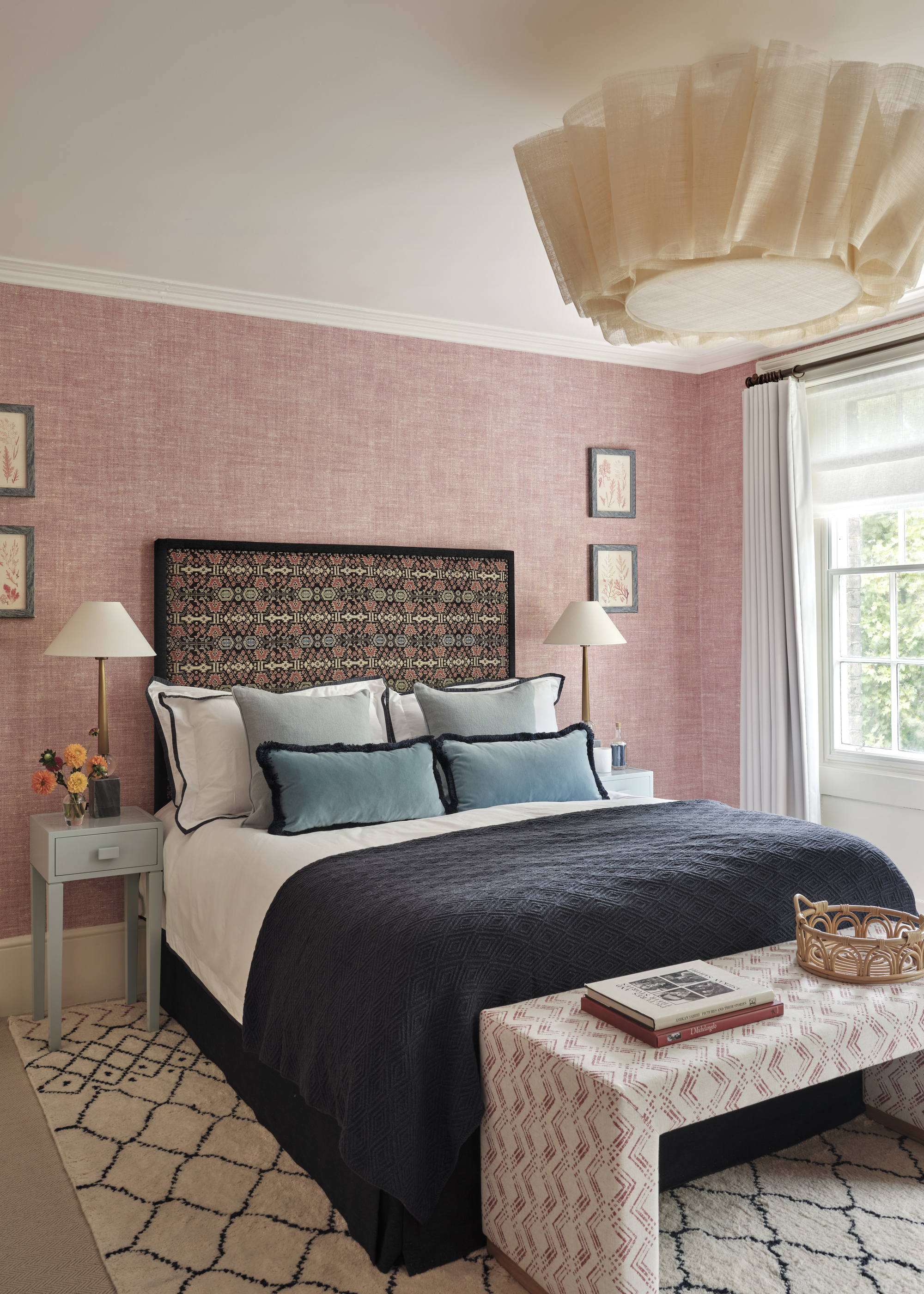 A bedroom with pink walls, a Berber rug, and a dressed bed with a navy throw