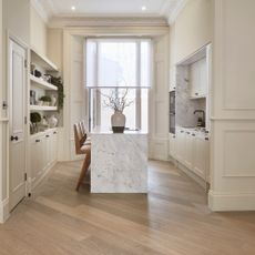 off white kitchen with shutters and voile blind at window, marble waterfall island, diagonal hardwood floor, black hardware and tap, open shelving