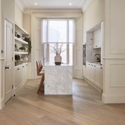 off white kitchen with shutters and voile blind at window, marble waterfall island, diagonal hardwood floor, black hardware and tap, open shelving