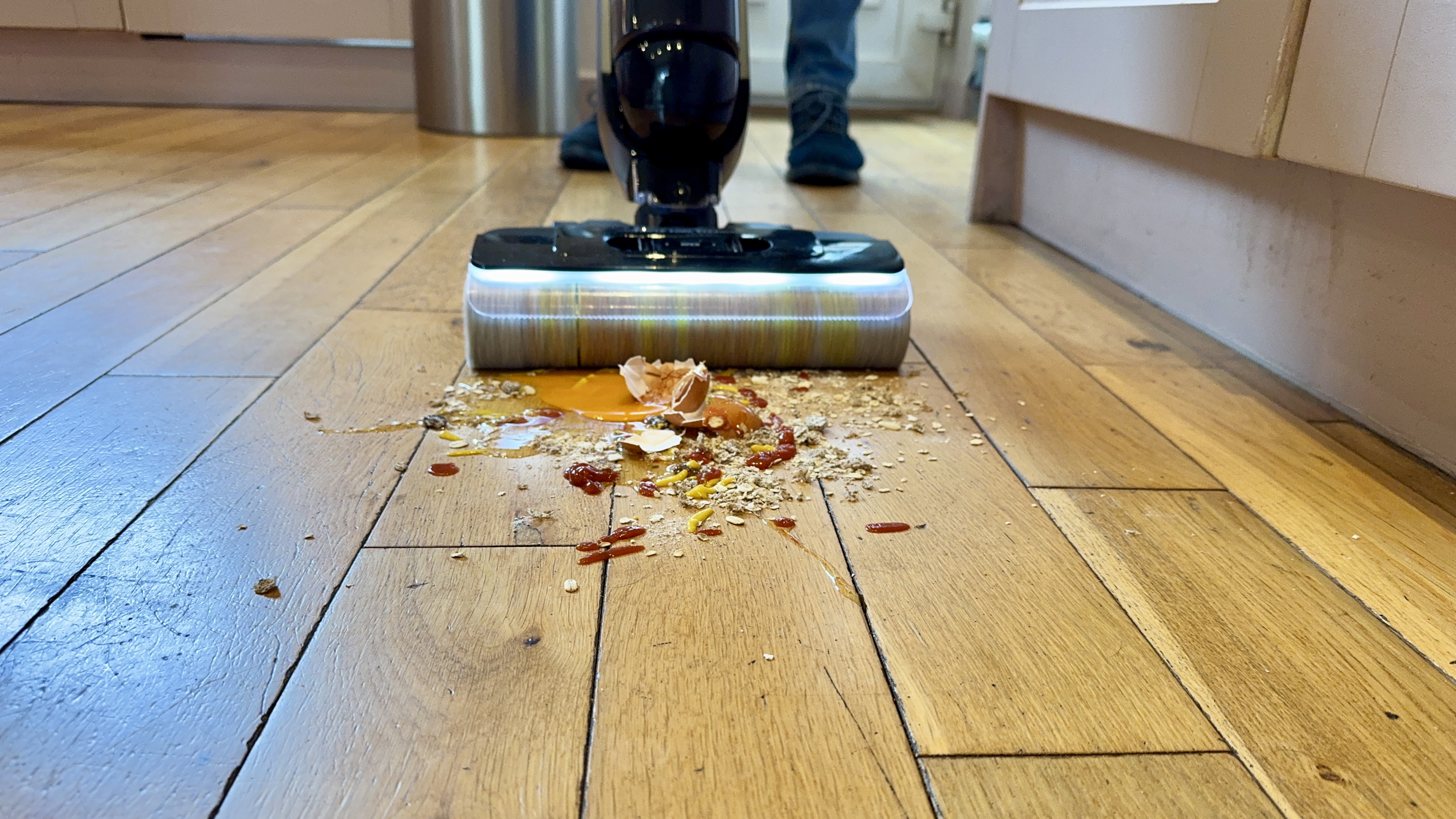 Eureka RapidWash 730 approaching a pile of oats, cracked egg, raisins and more on an engineered wood floor