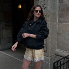 Eliza Huber wearing a sporty jacket, lace-trim shorts, and heeled sandals.