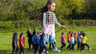 The larger-than-life puppet Little Amal performs as part of the Glastonbury Festival Global Livestream “Live at Worthy Farm”, walking through a field and flanked by real children who come up to her knees