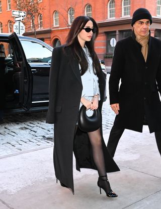 A photo of Mikey Madison pairing Ferragamo's black patent T-Bar Pumps with sheer black tights and St. Agni's spiraling black leather clutch.