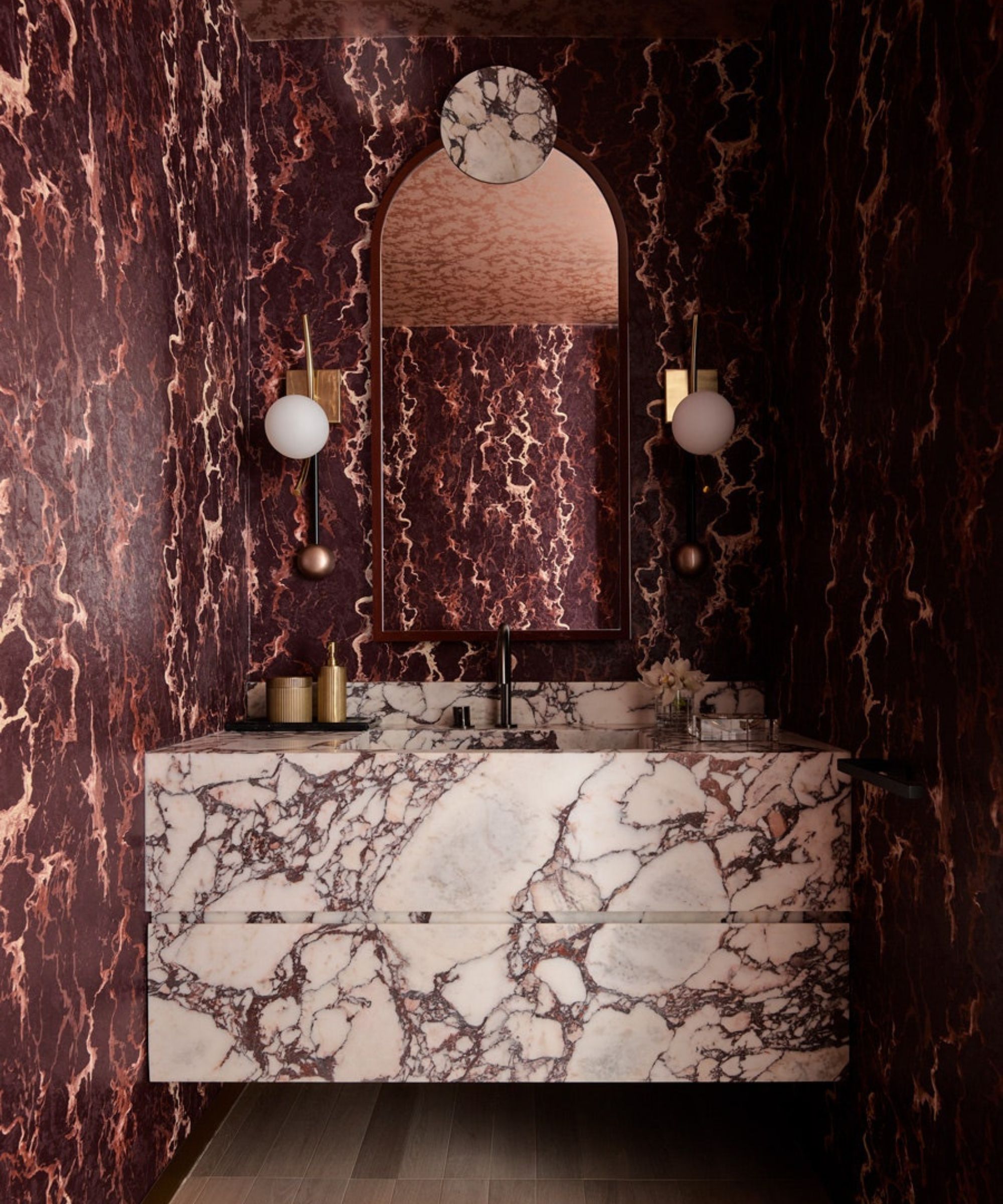 A dramatic bathroom vanity clad in bold veined marble, paired with sculptural lighting and deep-toned walls for a luxurious, statement finish.