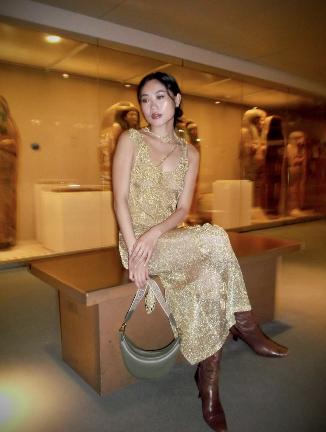 Vivian Li in a gold sparkly sheer dress, green bag, and brown boots