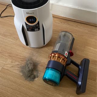 Shark NeverChange 5 Air Purifier sitting on the floor next to a pile of dust and a Dyson vacuum cleaner