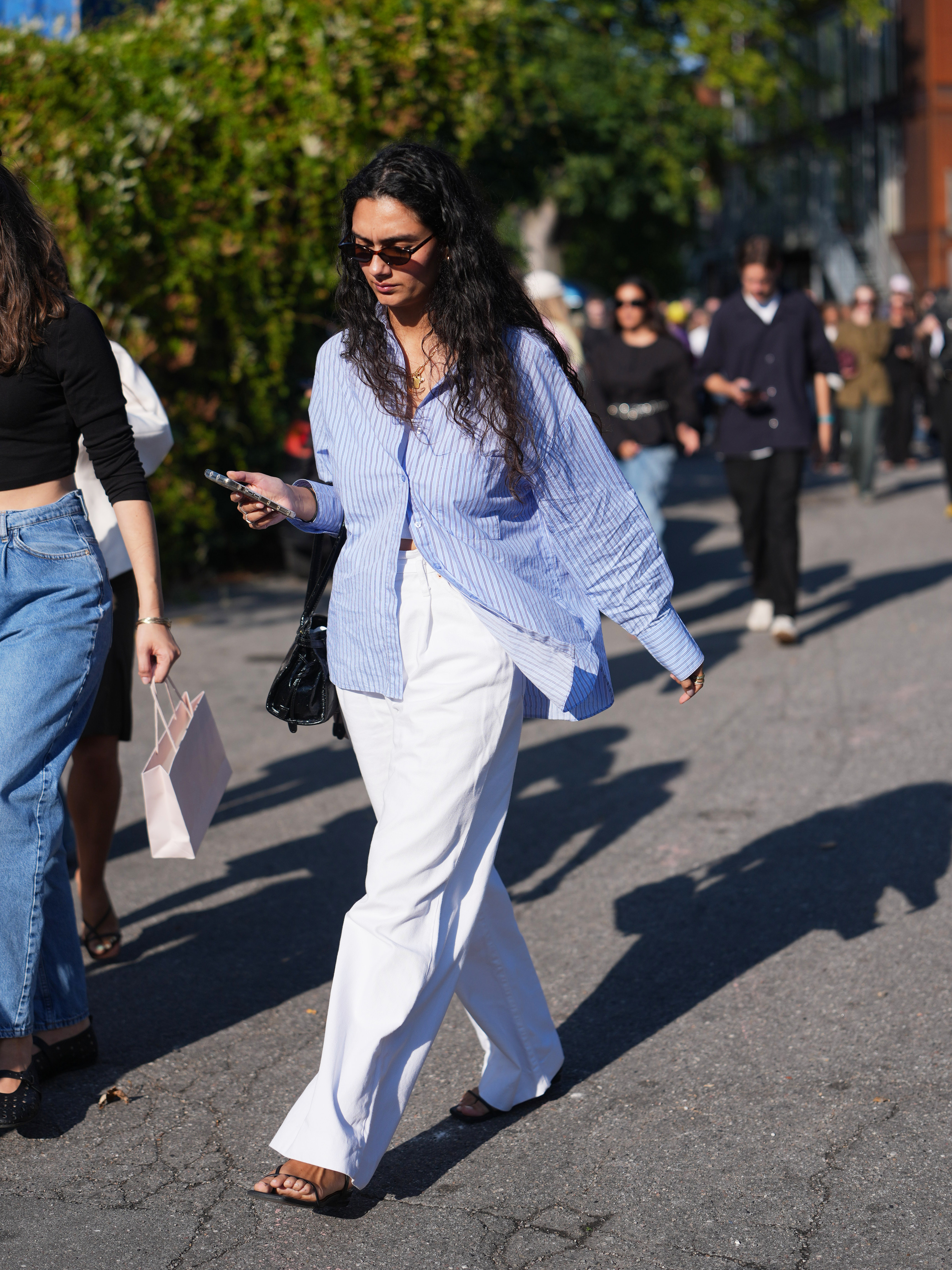 woman street style wearing white pants and a button down blue with black sunglasses