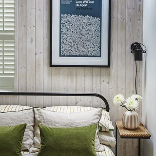 bed with green cushions in front of wooden cladded wall with artwork