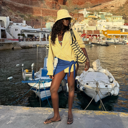 Influencer Amy Julliette Lefévre wearing a yellow stripe shirt, blue pareo, bucket hat, straw bag and thong sandals. 