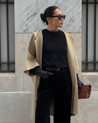 Woman wears camel coat, black knit, black trousers, black gloves