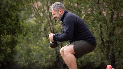 Man squatting with kettlebell outside, his face screwed up