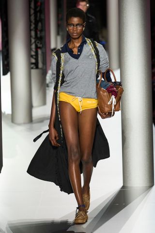 A model wearing Miu Miu's boat shoes, yellow swim trunks, grey sweater, blue polo, on its Spring 2024 runway