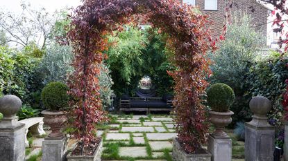 garden arch ideas – leafy arch on modern patio with mirror and dining set