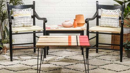 A pallet coffee table with metal hairpin legs with two black chairs in background